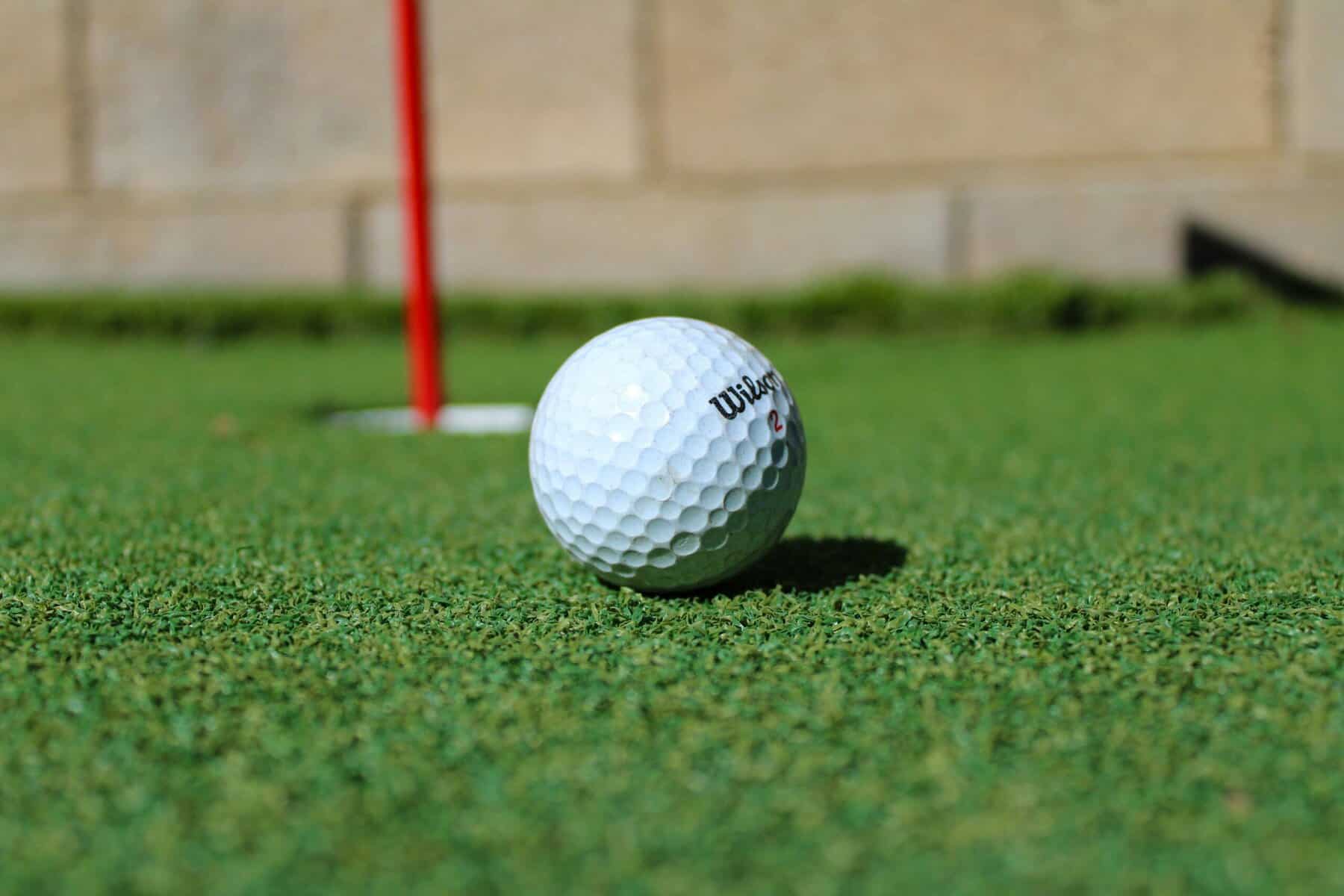 Golf putting green turf with golf ball and flagstick in view. Beautiful artificial golf course turf for realistic putting experience and landscape design.
