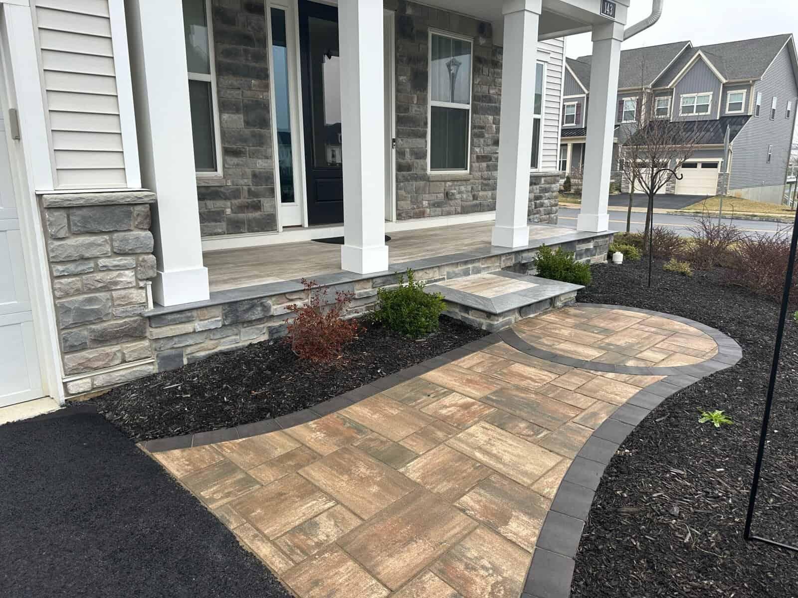 Landing and pathway landscape design for home entrance. Beautiful stone and paver walkway with garden beds and steps in front porch area.
