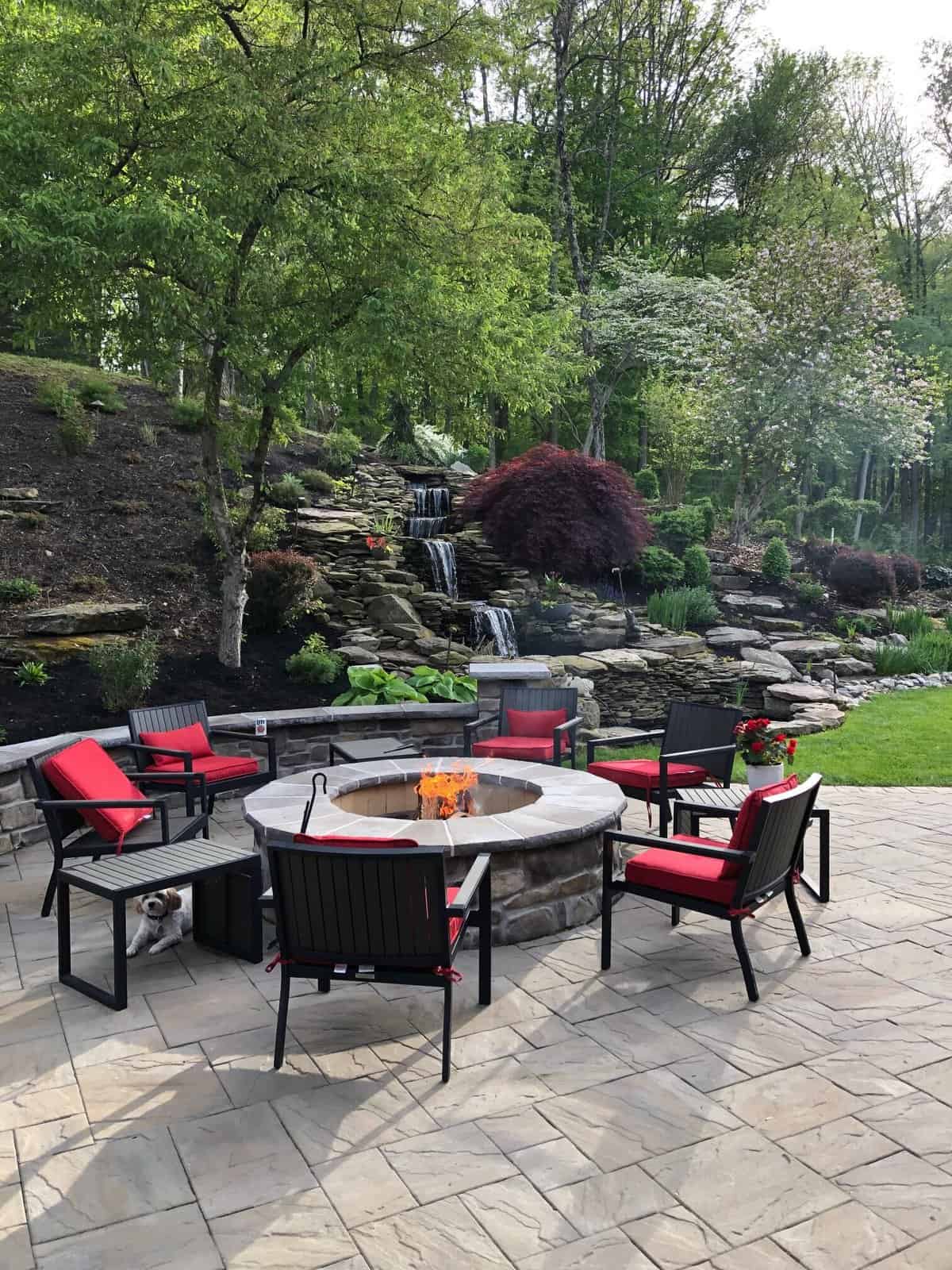 Cozy-Wood-Burning-Fire-Pit-Design Round wood burning stone fire pit on textured paver patio in West Chester backyard