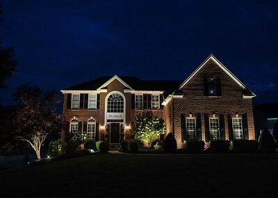 Nighttime view of large brick front estate home illuminated by architectural landscape lighting in West Chester PA