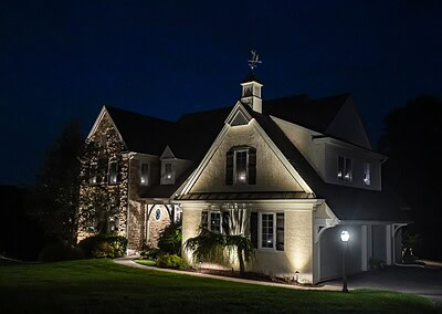 Nighttime landscape lighting on luxury home with stucco and natural stone facade in West Chester PA